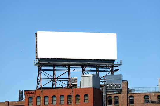 A large blank billboard on a rooftop against a blue sky