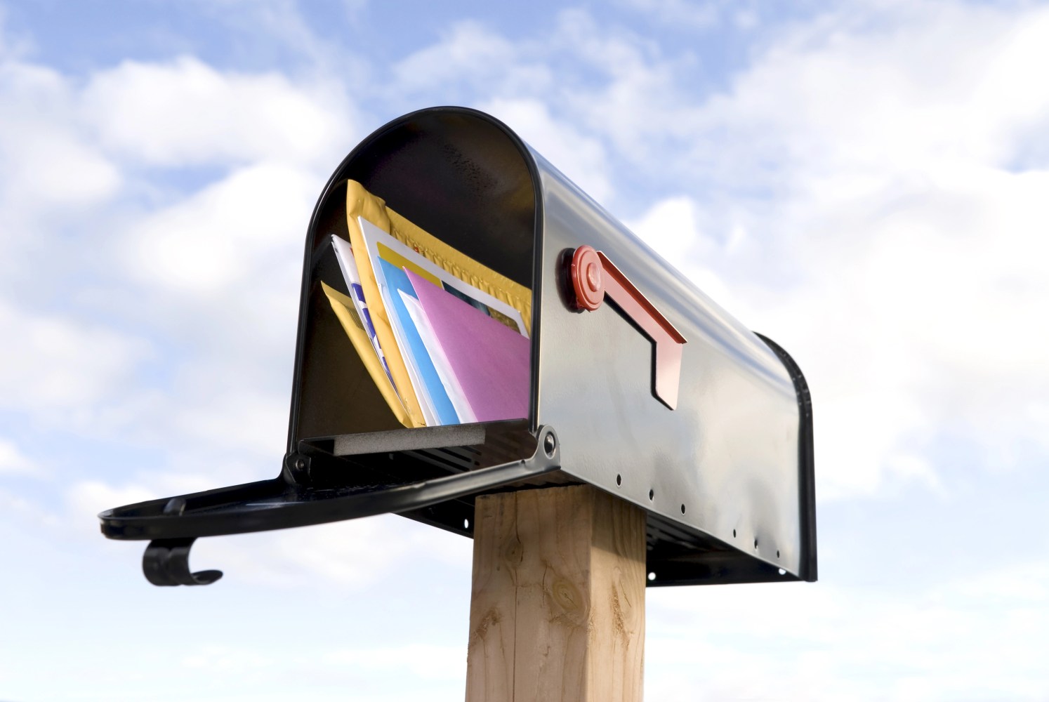 An open mailbox holding several envelopes against a blue sky